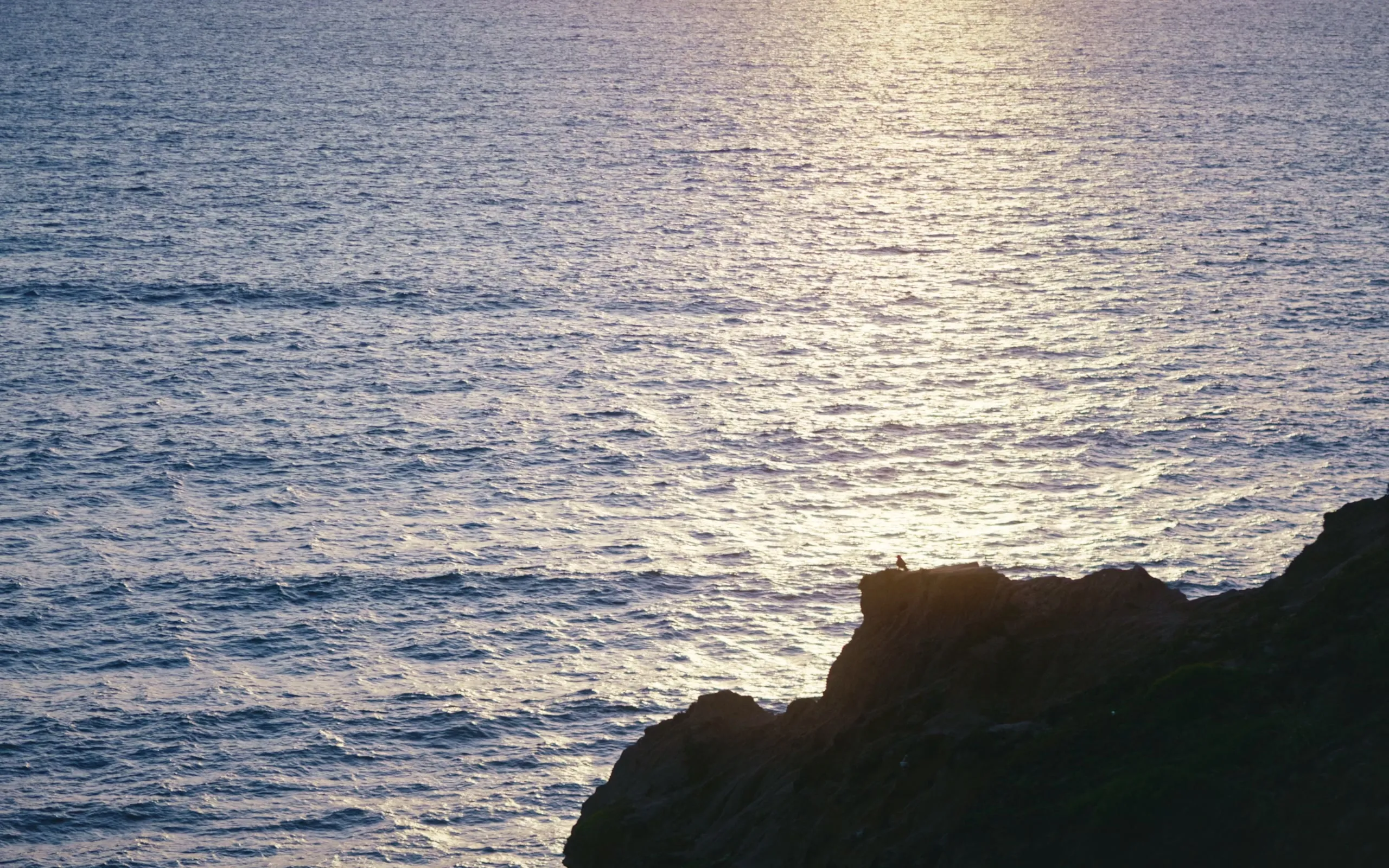 Late sun scattered across the water past a headland rock